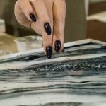 a girl with a black manicure pours a hard transparent crumb on an epoxy painting